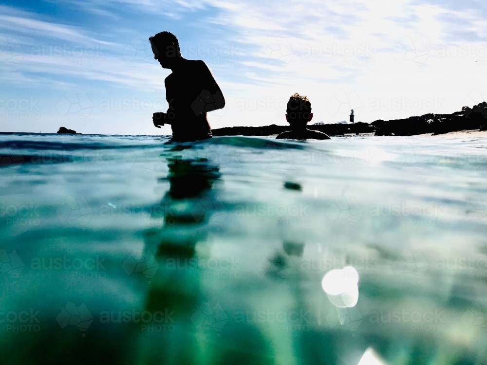 Man and boy at sunrise swimming in the aqua waters of the ocean - Australian Stock Image