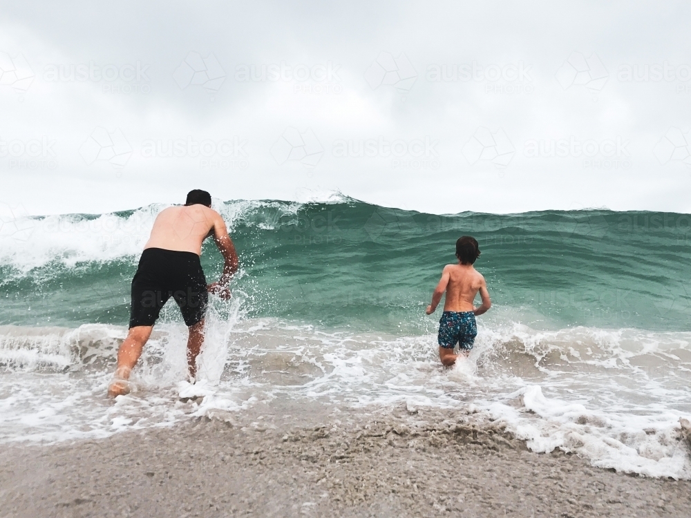 Man and boy diving into waves at the beach - Australian Stock Image