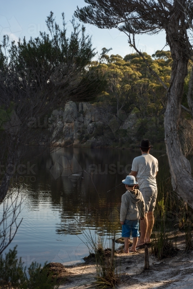 Man and boy fishing at river outlet with sun ray light - Australian Stock Image