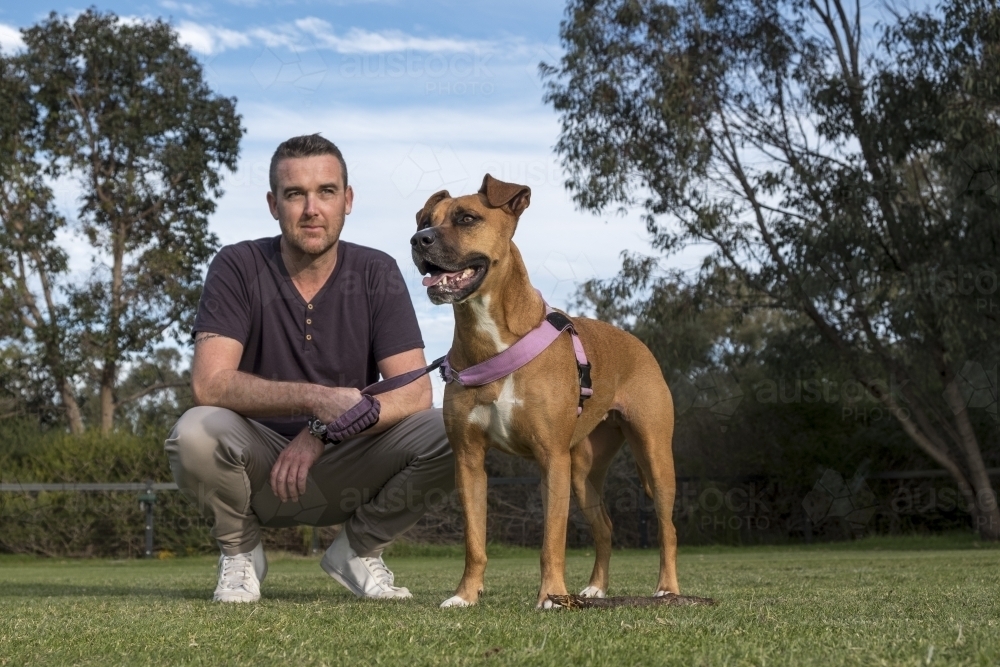 Man and Crossbreed Dog Squatting in Park - Australian Stock Image