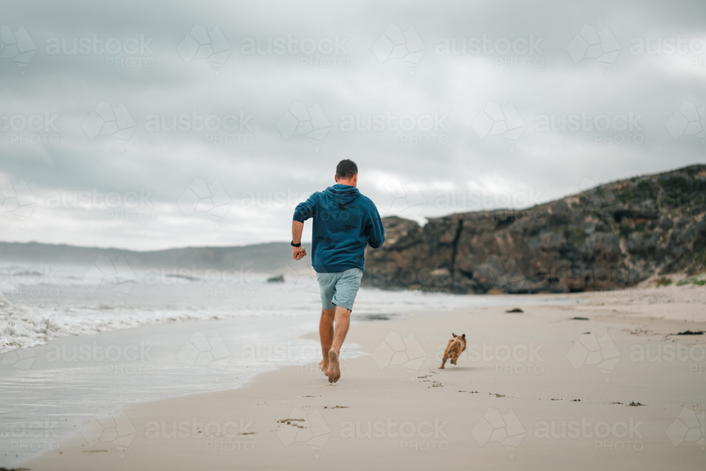 Man and dog running on the beach in Portland, Victoria - Australian Stock Image