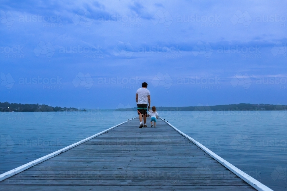 Man and kid walking down Warners Bay Public Jetty in dusk light - Australian Stock Image