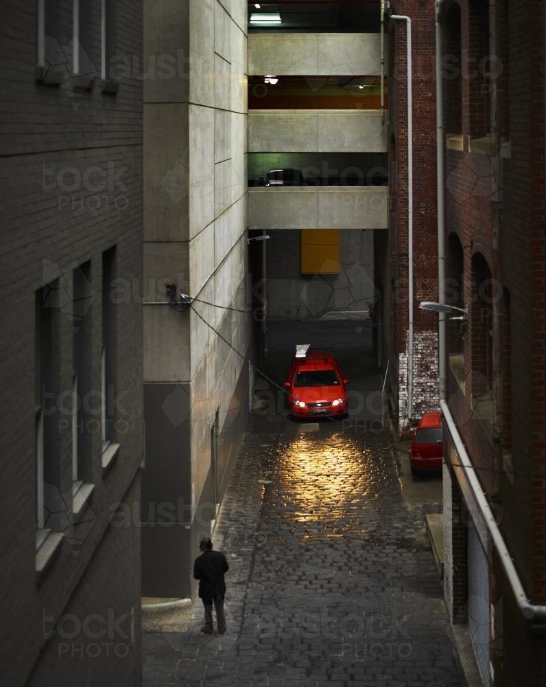 Man and red car with headlights on in city lane - Australian Stock Image