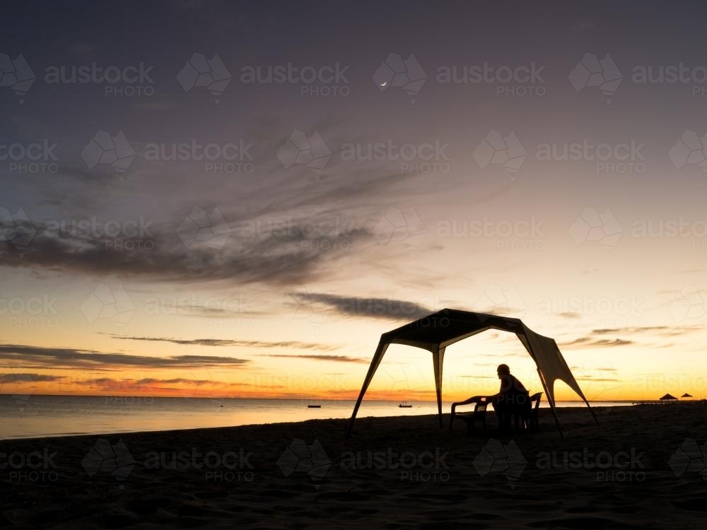 Man and tent silhouetted against sunset on a beach - Australian Stock Image