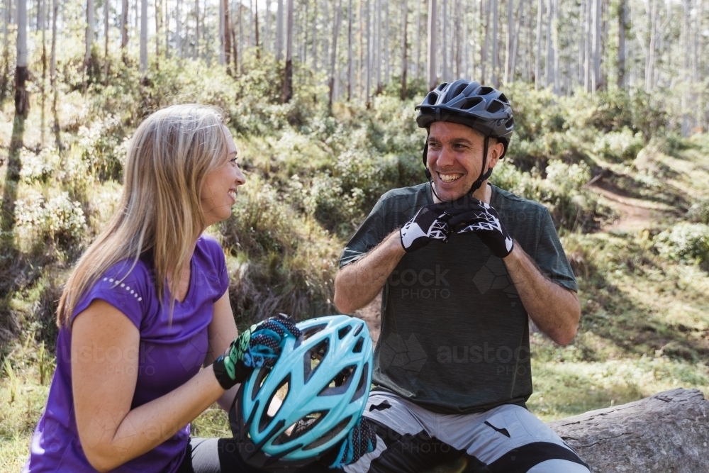 Man and woman biker sitting fixing their helmets in bushland - Australian Stock Image