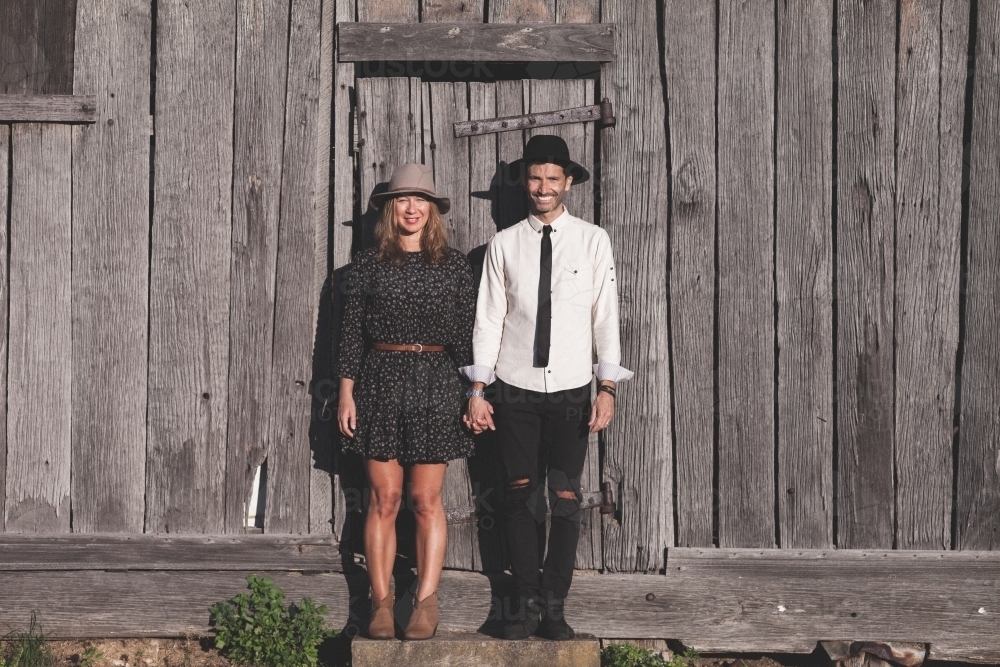 Man and woman holding hands standing against rustic wooden wall - Australian Stock Image