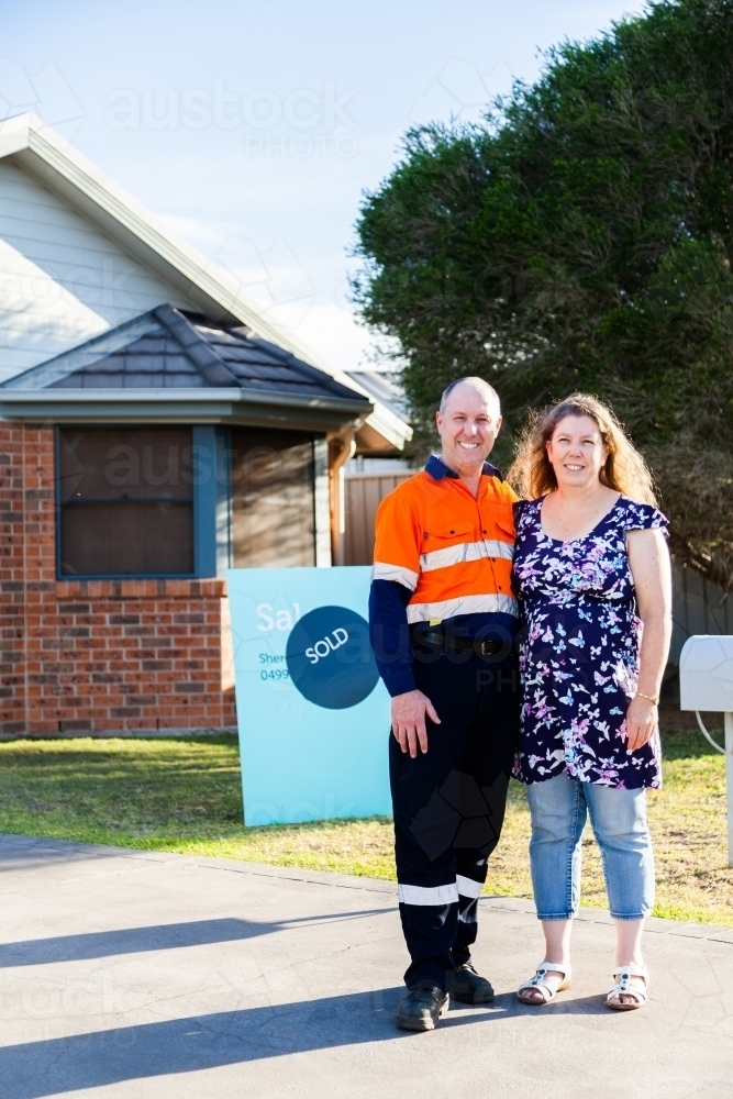 Man and woman in front of investment property house with sold sign - Australian Stock Image