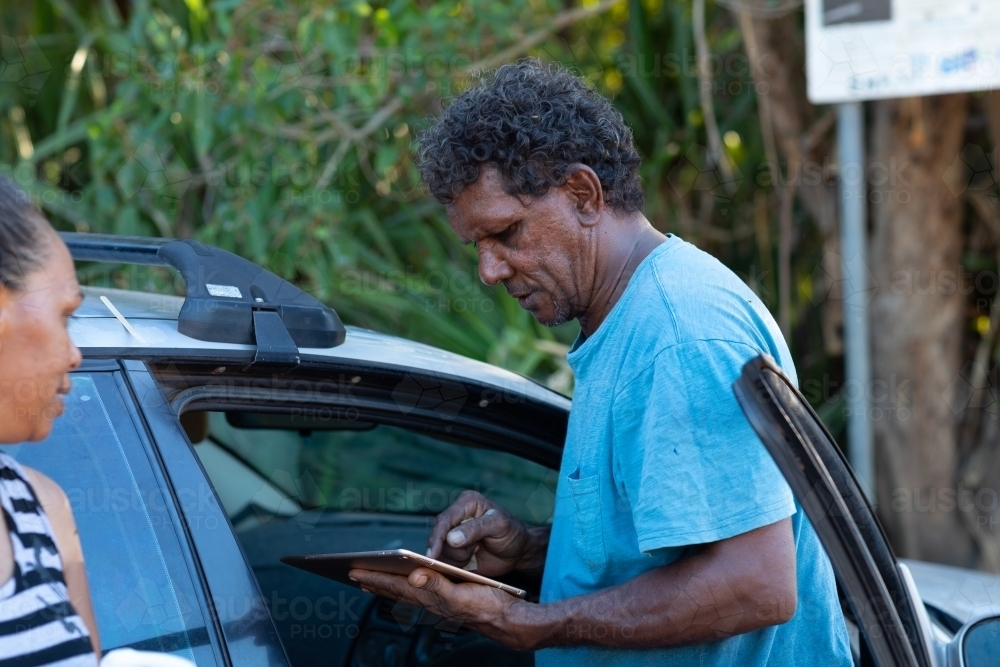 man and woman next to car with man looking at digital tablet - Australian Stock Image
