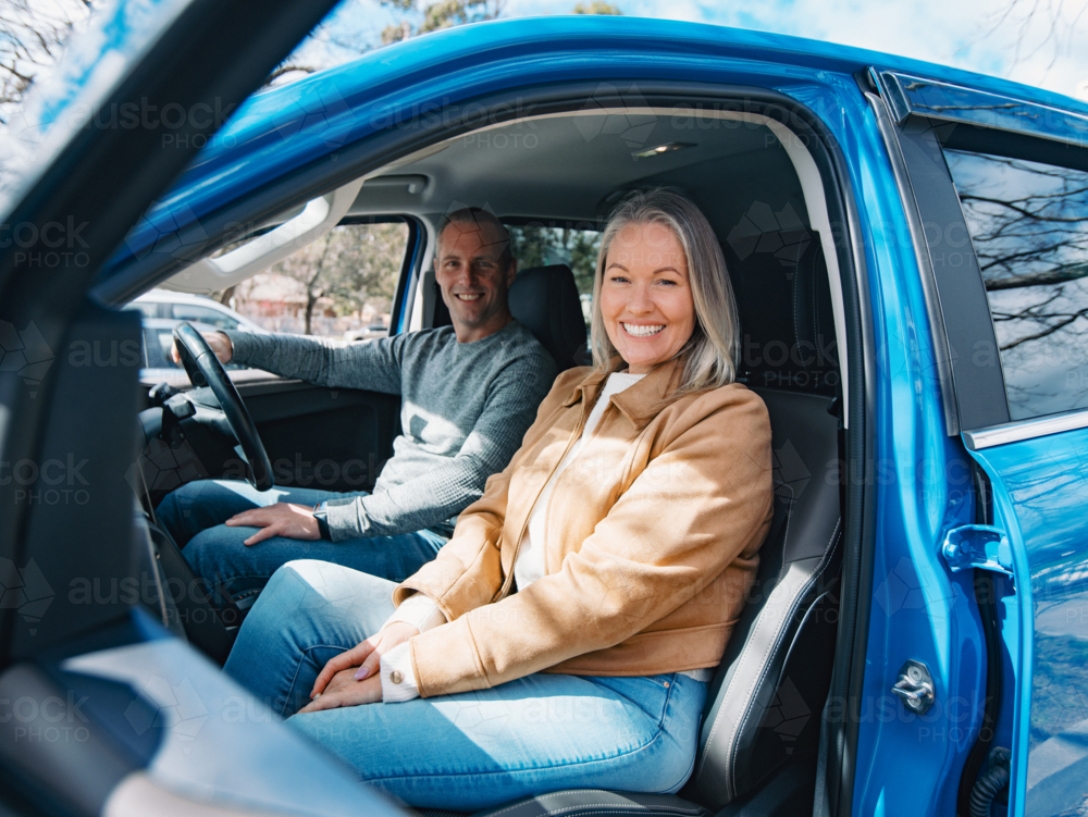 Man and woman seated inside blue car smiling - Australian Stock Image