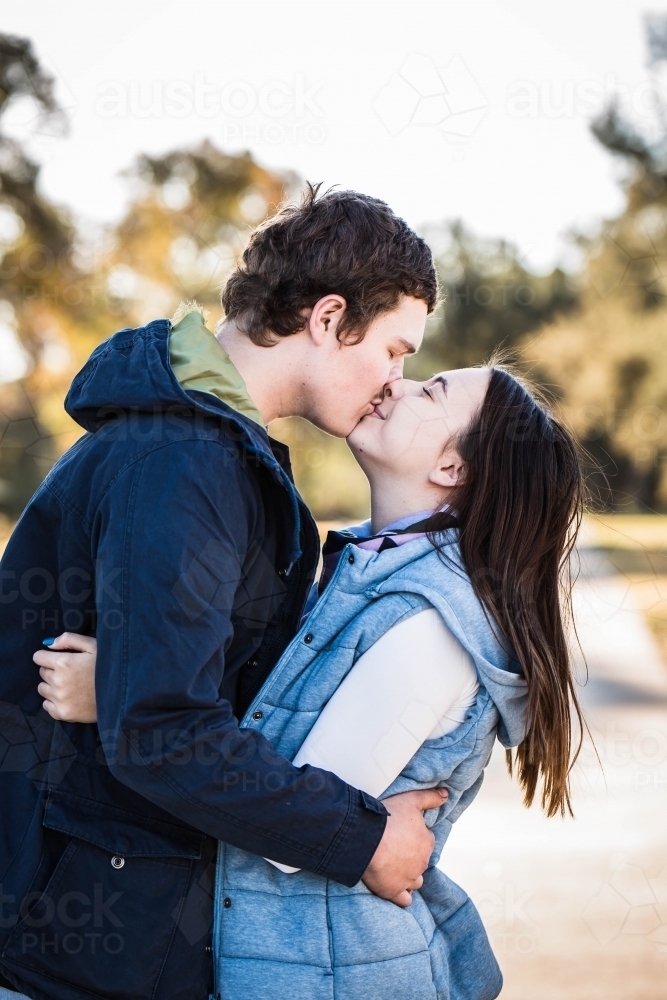 Man and woman standing arm in arm kissing - Australian Stock Image