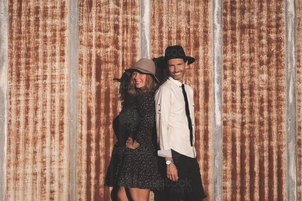 Man and woman standing back to back against rusted iron wall - Australian Stock Image
