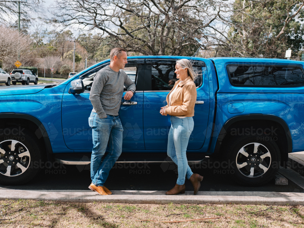 Man and woman standing beside parked blue car outdoors - Australian Stock Image