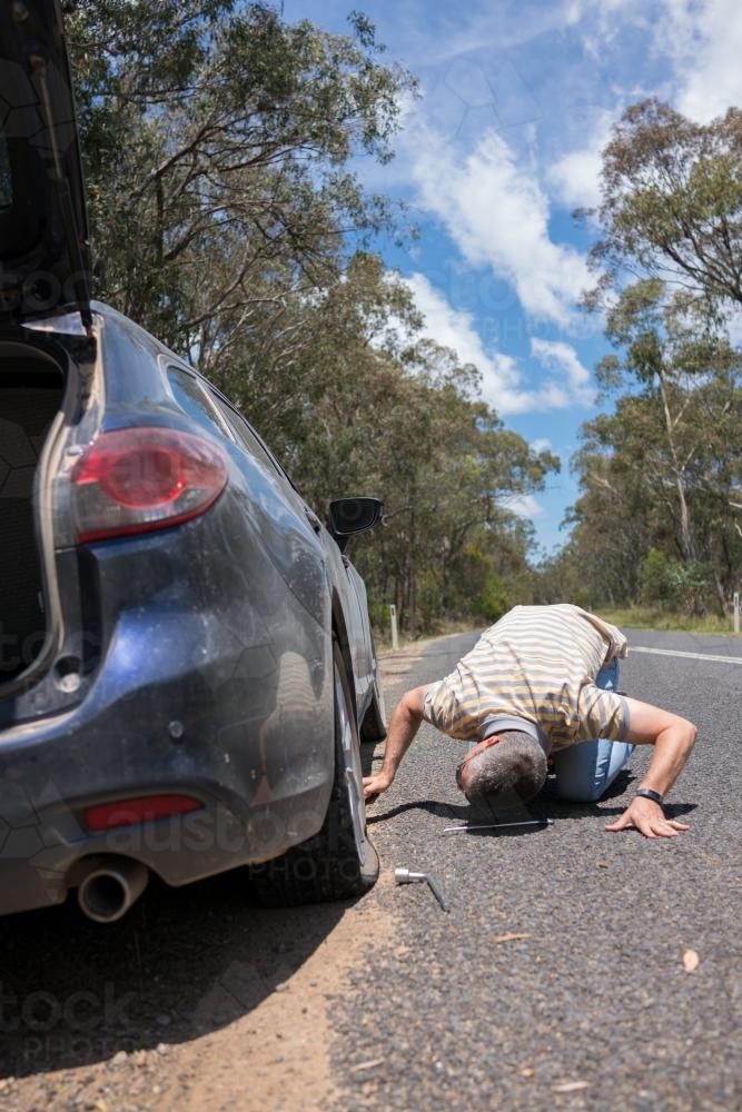 Man changes a tyre after getting a flat tyre on a country road - Australian Stock Image