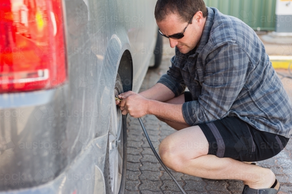 man checking and filling tyres at service station - Australian Stock Image