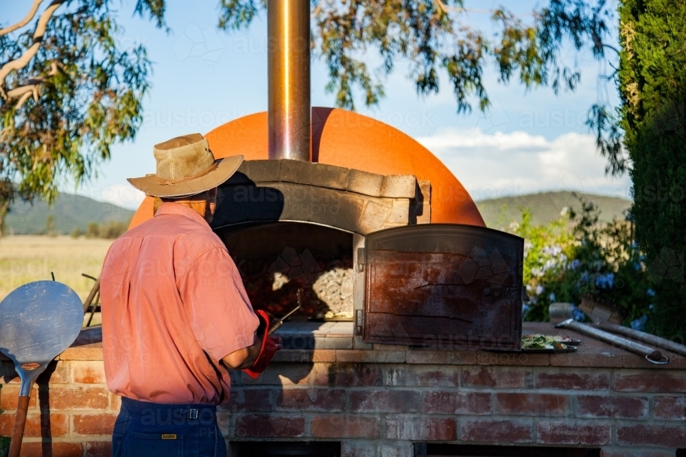 Man cooking home made pizza in outdoor pizza oven - Australian Stock Image