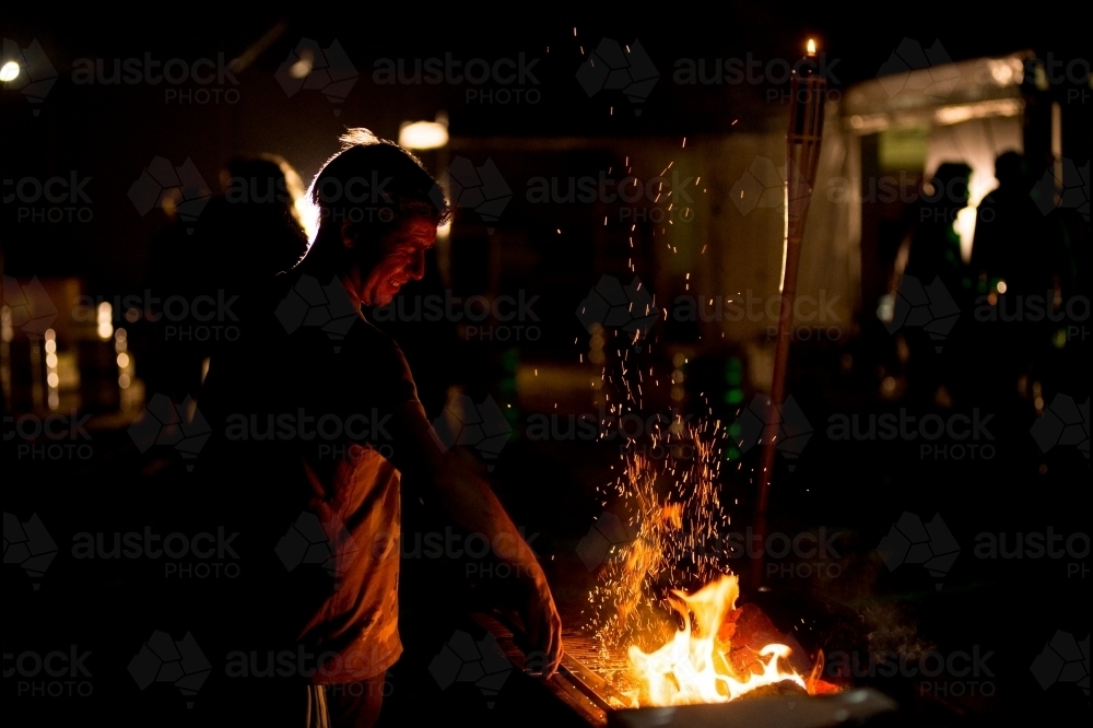 Man cooking on a BBQ at night - Australian Stock Image