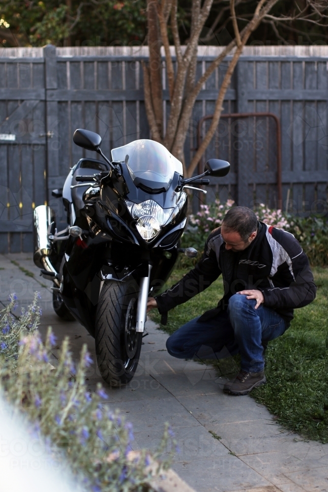 Man crouching next to motorbike in garden - Australian Stock Image
