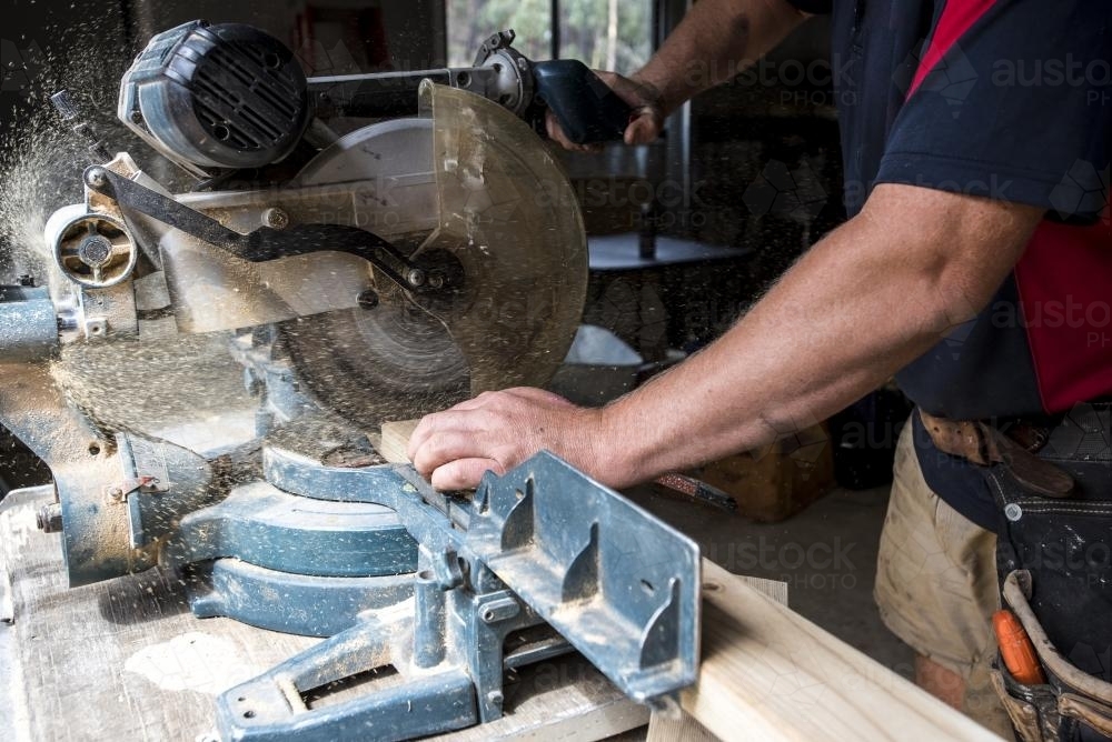 Man cutting timber with drop saw with sawdust coming out of saw - Australian Stock Image