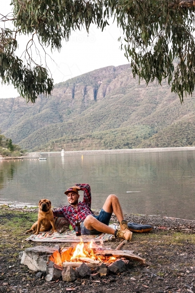 Man & dog enjoying open fire by the dam - Australian Stock Image