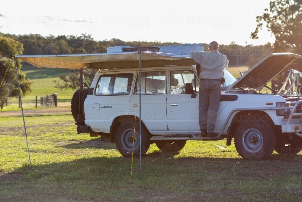 man doing work on old 4wd wagon with awning - Australian Stock Image