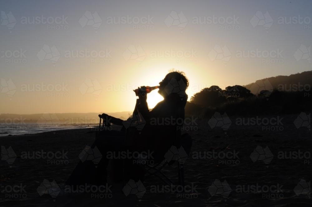 Man drinking from a bottle, silhouetted against low light sky - Australian Stock Image