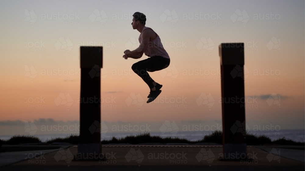Man exercising by jumping in air beside ocean - Australian Stock Image