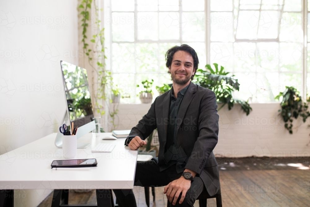 Man facing a camera sitting at a desk in a creative warehouse studio - Australian Stock Image