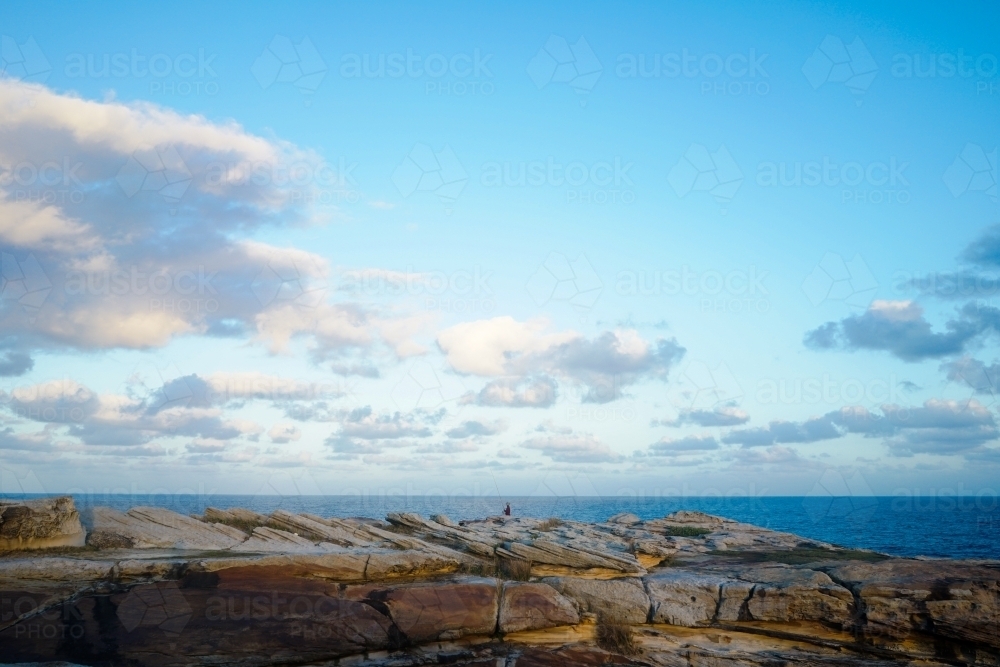 Man fishing alone from a cliff of rocks beside the ocean - Australian Stock Image
