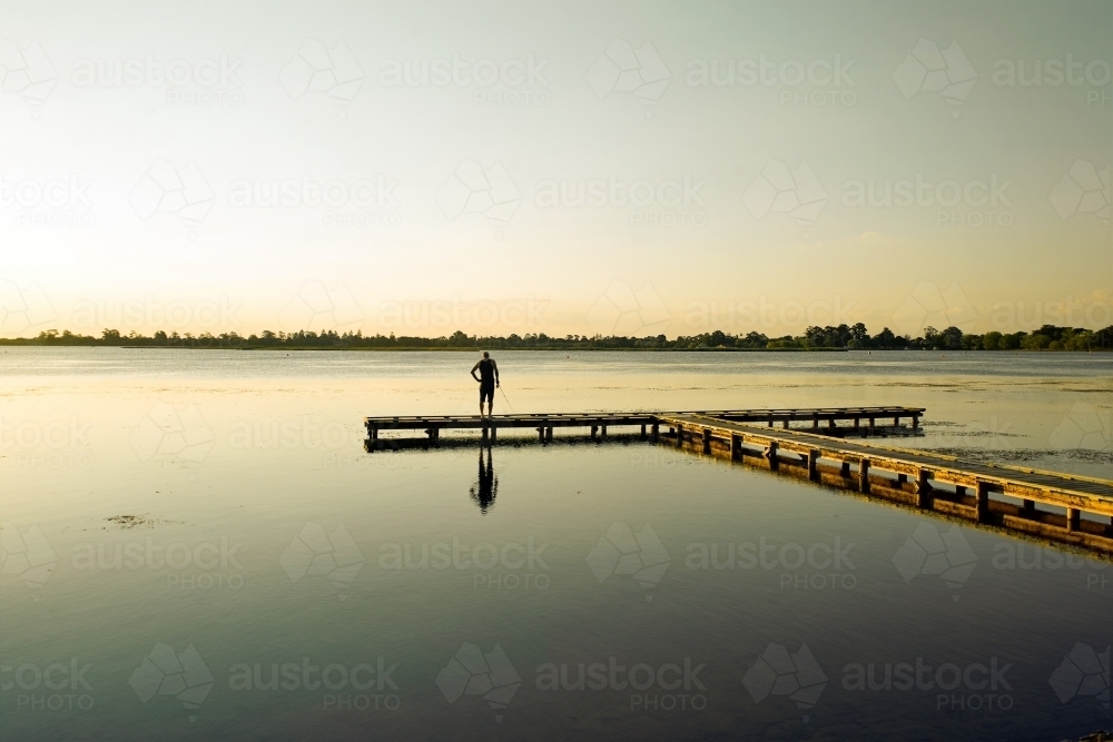 Man fishing at a lake from a jetty - Australian Stock Image