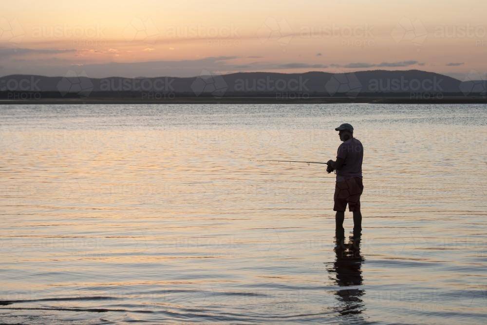 Man fishing in shallow water at dusk - Australian Stock Image