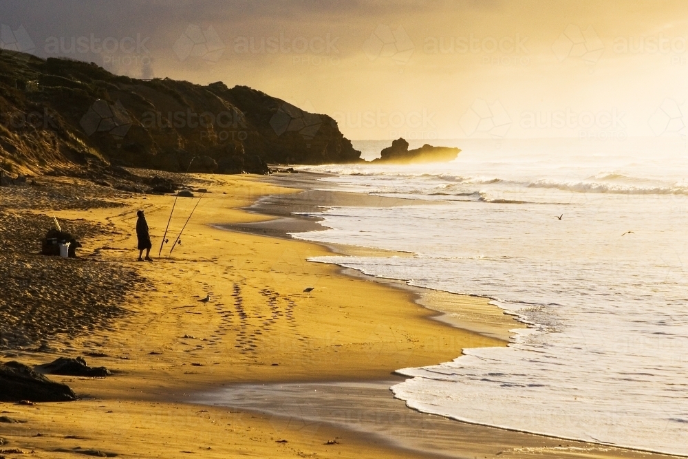 Man fishing on beach at dusk - Australian Stock Image