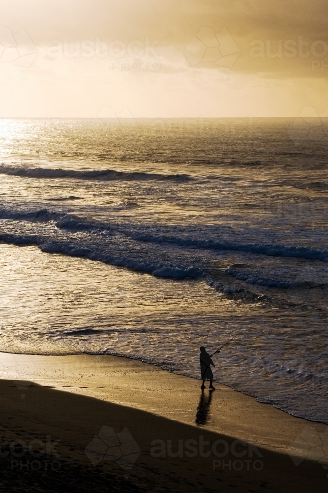 Man fishing on beach at dusk - Australian Stock Image