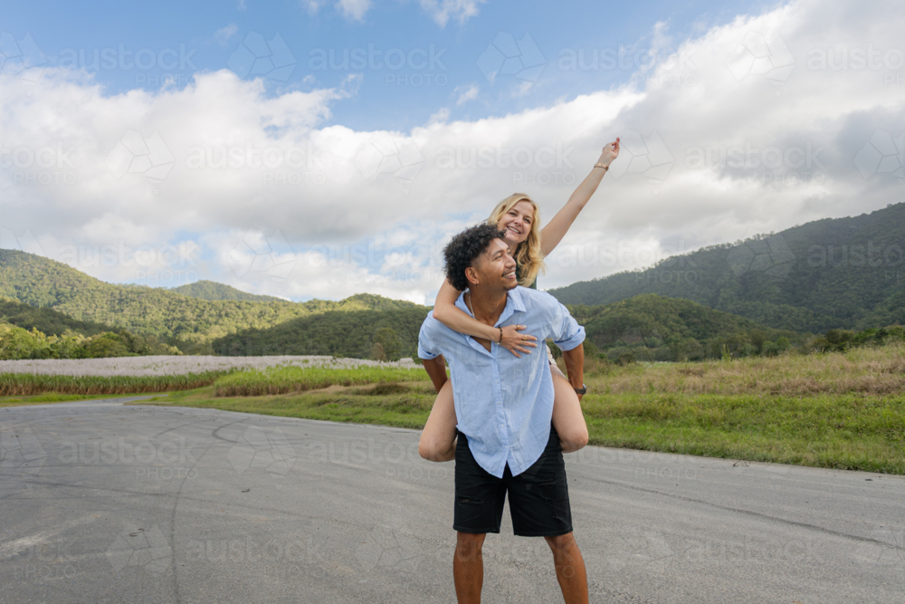Man gives a woman a piggyback ride on a country road in Queensland - Australian Stock Image