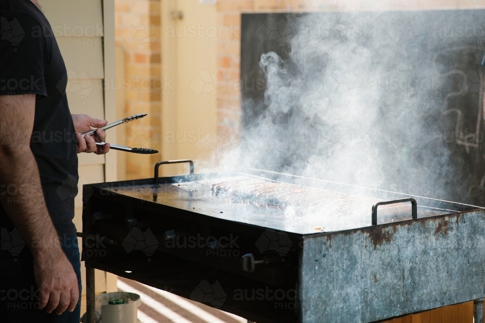 Man grilling and holding a tong in front of a smoking griller - Australian Stock Image