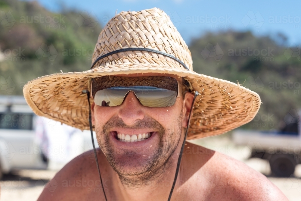 man grinning in straw hat at the beach - Australian Stock Image