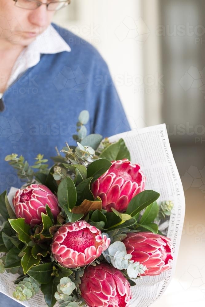 Man holding a bunch of pink flowers and leaves wrapped in paper - Australian Stock Image