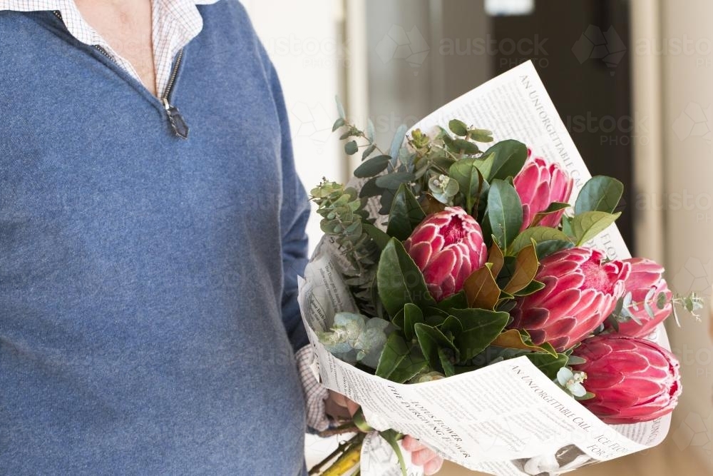Man holding a bunch of pink native flowers and leaves wrapped in paper - Australian Stock Image