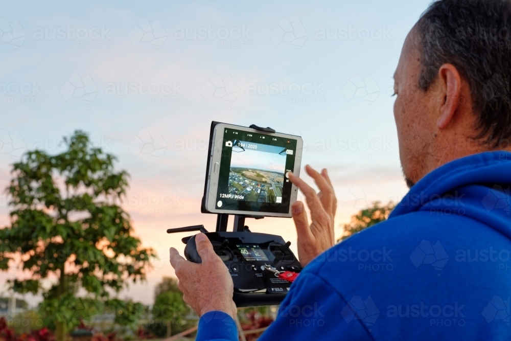 Man holding a controller with screen on watching the drone, UAV, RPAs in flight - Australian Stock Image