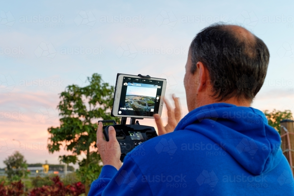 Man holding a controller with screen on watching the drone, UAV, RPAs in flight - Australian Stock Image