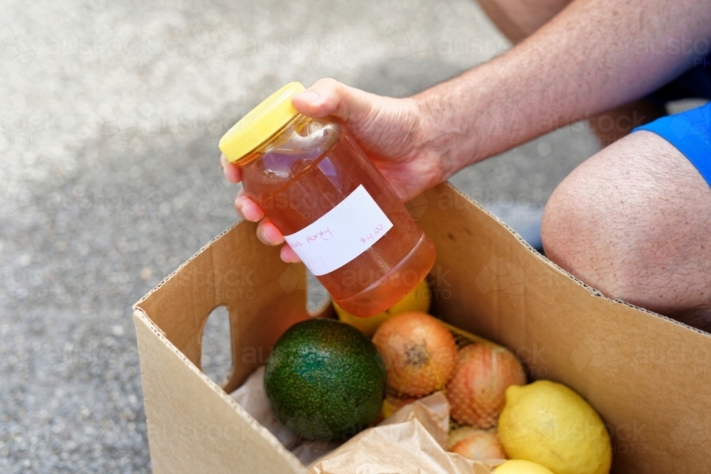 Man holding a jar of honey from a box filled with fresh produce containing lemon, onions and avocado - Australian Stock Image