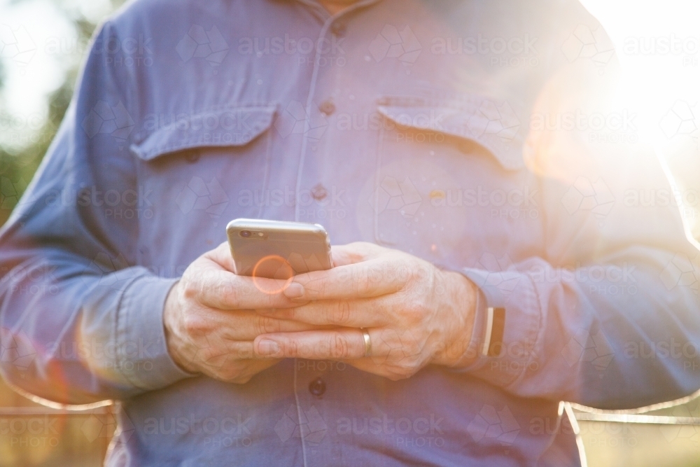 Man holding iPhone outside with lens flare - Australian Stock Image