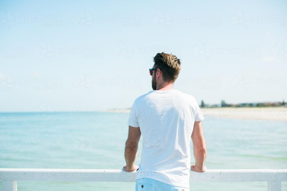 Man holding onto jetty railing overlooking water - Australian Stock Image