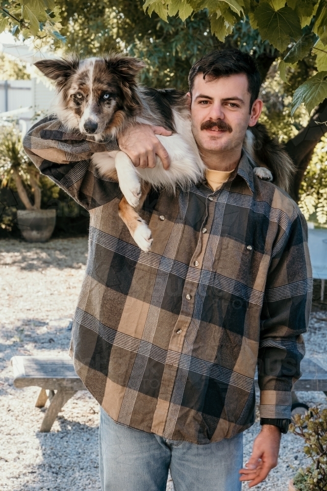 Man holding pet dog on his shoulders. - Australian Stock Image