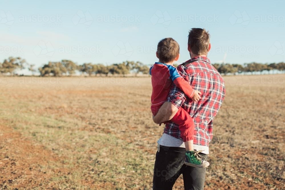 Man holding toddler walking in a paddock - Australian Stock Image