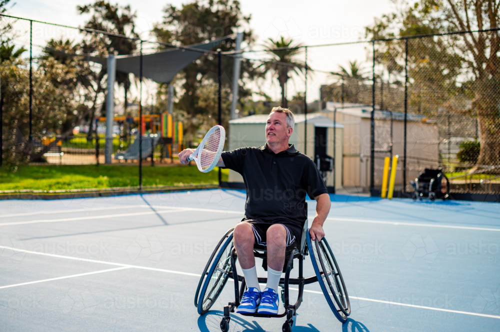 Man in a wheelchair participates in tennis practice on a bright day - Australian Stock Image