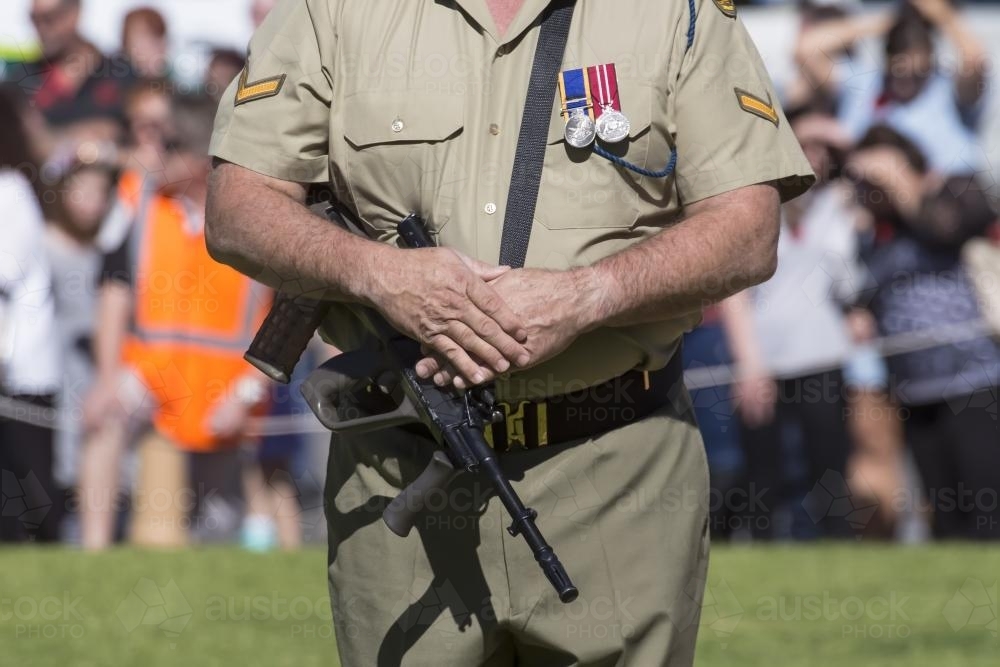 Man in army uniform with rifle participating in ANZAC Day ceremony - Australian Stock Image