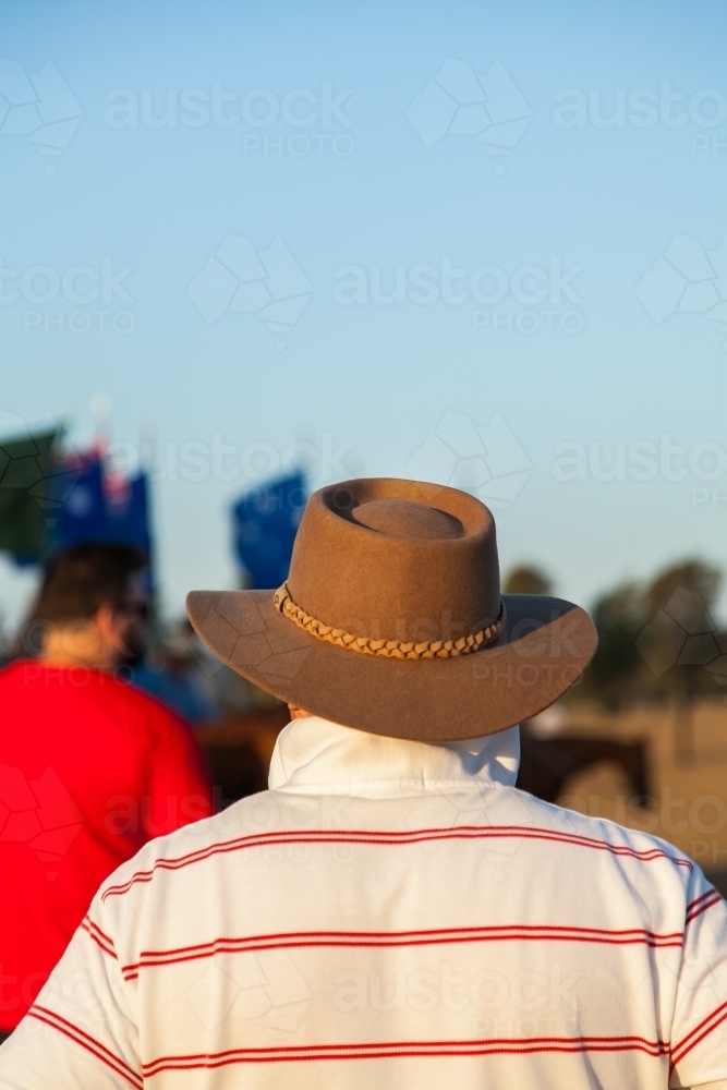 Man in brown hat watching horsemen with Australian flags - Australian Stock Image