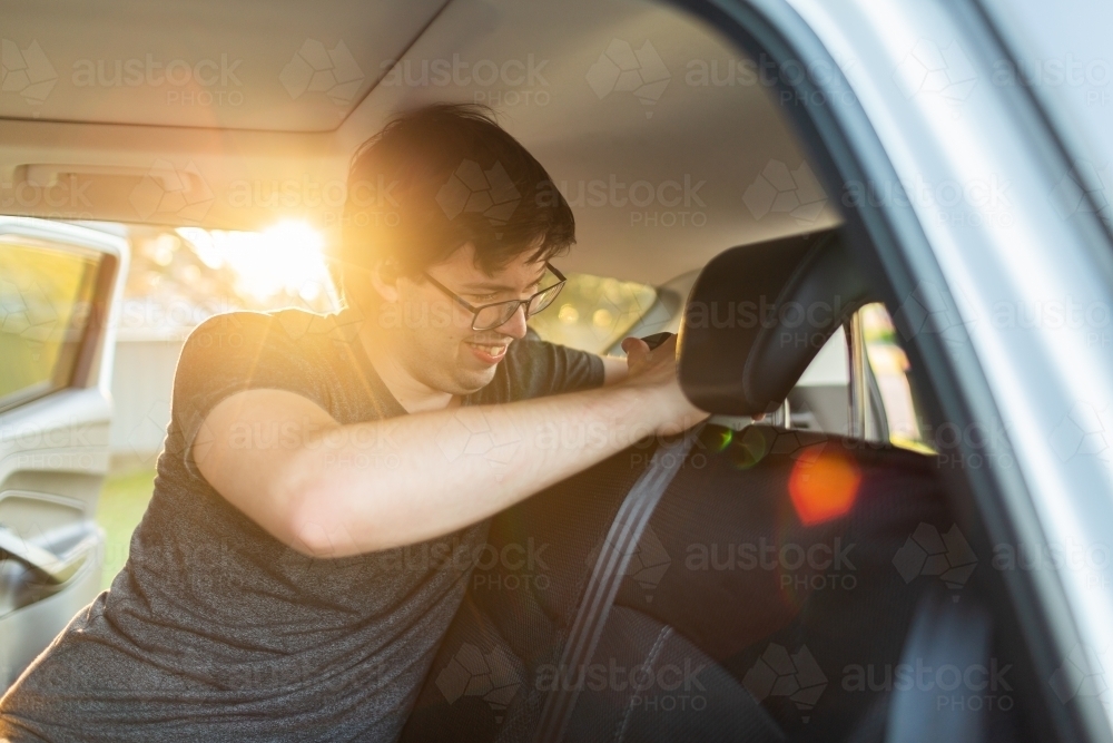 Image of Man in car putting seat covers on back seat while listing to
