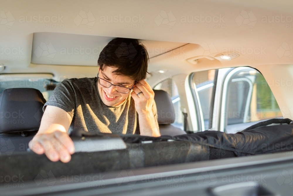 Image of Man in car putting seat covers on back seat while listing to