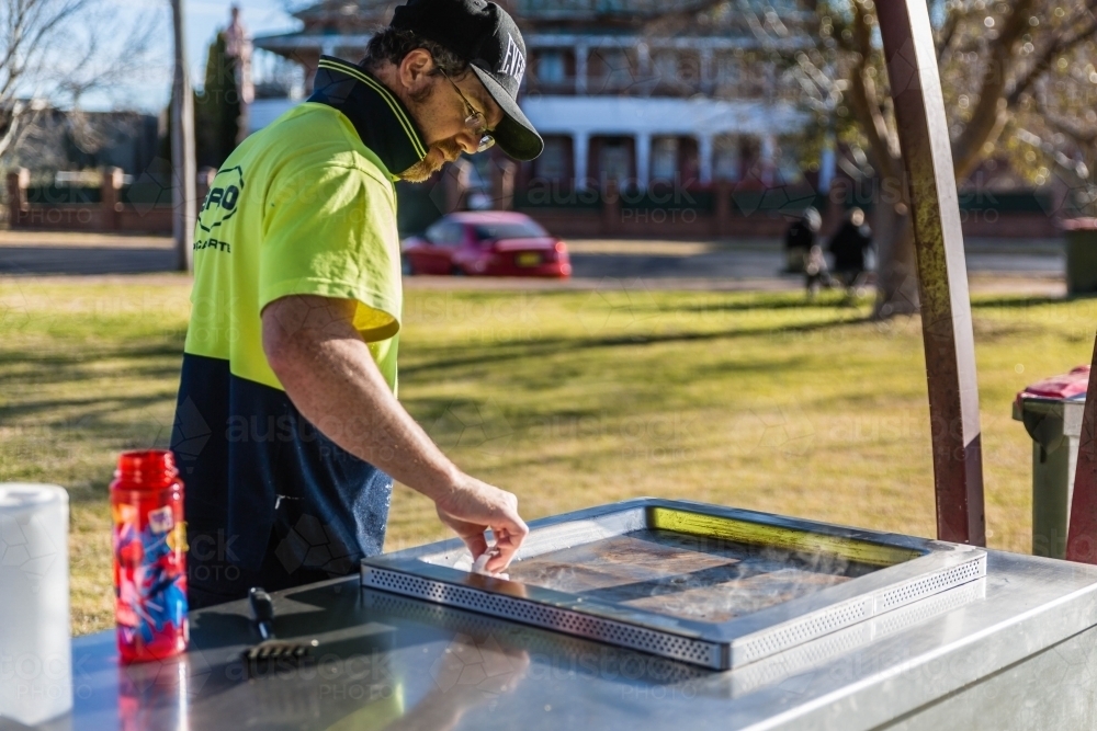 Man in hat cleaning barbecue - Australian Stock Image